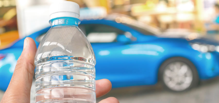 A hand holding a bottle of water with a blue car in the background. A single small bottle of water is never enough.